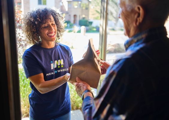 Volunteer walking up to door of client smiling before handing over the meal.
